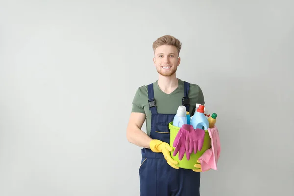 Portrait of male janitor with cleaning supplies on light background — Stock Photo, Image