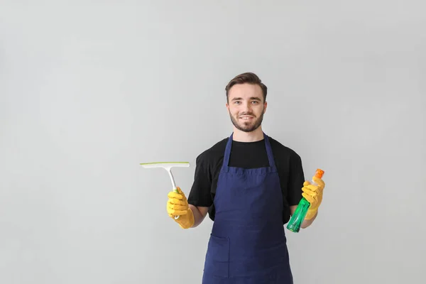 Portrait of male janitor with cleaning supplies on light background — Stock Photo, Image