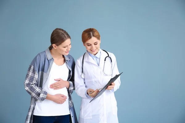 Gynecologist with young pregnant woman on grey background — Stock Photo, Image