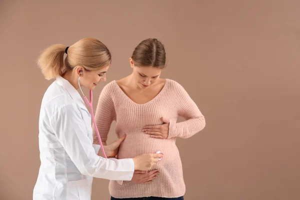 Gynaecoloog onderzoekt jonge zwangere vrouw op kleur achtergrond — Stockfoto