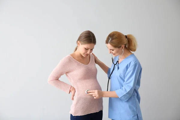 Gynekolog undersöker ung gravid kvinna på ljus bakgrund — Stockfoto