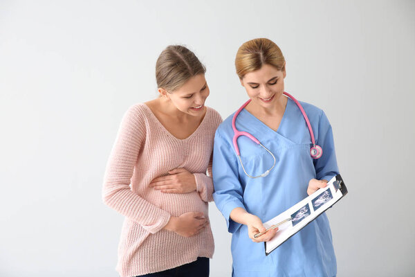 Гинеколог с молодой беременной женщиной на светлом фоне
