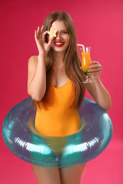 Piękna młoda kobieta z nadmuchiwanym pierścieniem i koktajlem na kolorowym tle — Zdjęcie stockowe