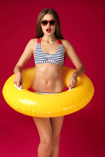 Surprised young woman with inflatable ring on color background — Stock Photo, Image