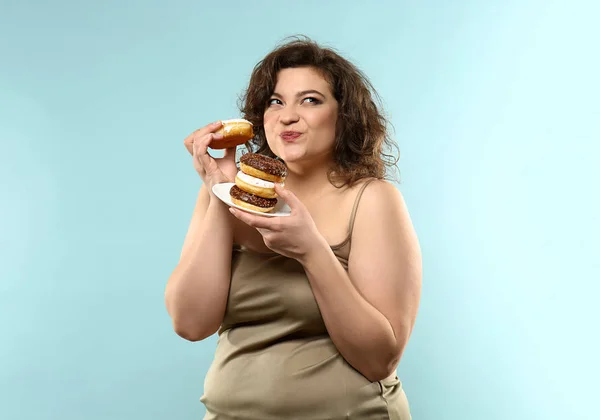 Overgewicht vrouw met donuts op kleur achtergrond — Stockfoto