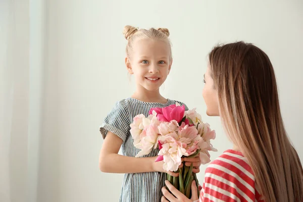 Маленькая девочка приветствует свою мать букетом тюльпанов дома — стоковое фото