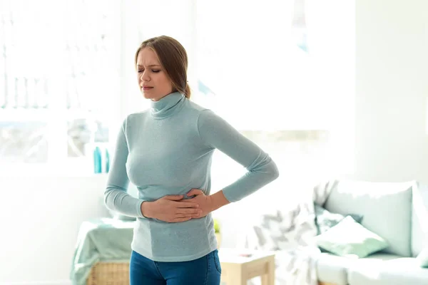 Mujer joven que sufre de dolor de estómago en casa —  Fotos de Stock