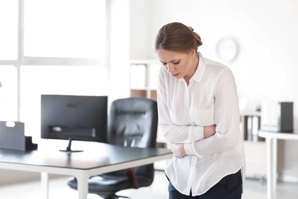 Young woman suffering from stomachache in office — Stock Photo, Image