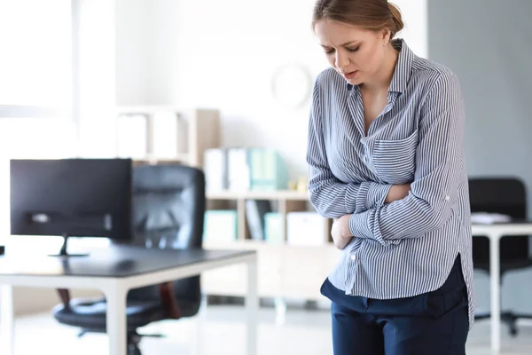 Młoda kobieta cierpiąca z powodu ból brzucha w biurze — Zdjęcie stockowe