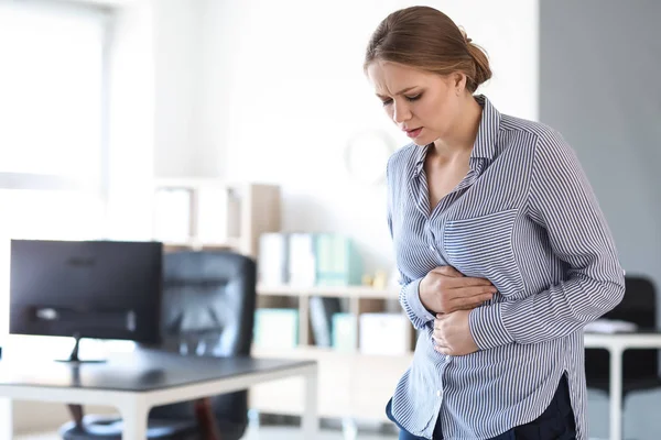 Young woman suffering from stomachache in office — Stock Photo, Image