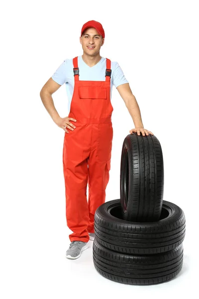 Jeune mécanicien masculin en uniforme avec des pneus de voiture sur fond blanc — Photo