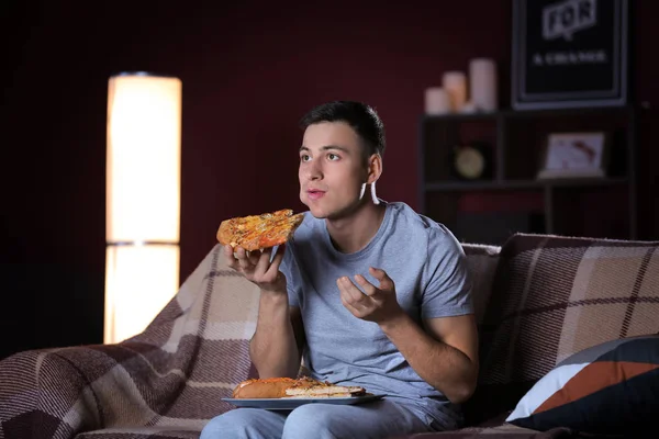 Joven guapo comiendo comida poco saludable mientras ve la televisión por la noche — Foto de Stock