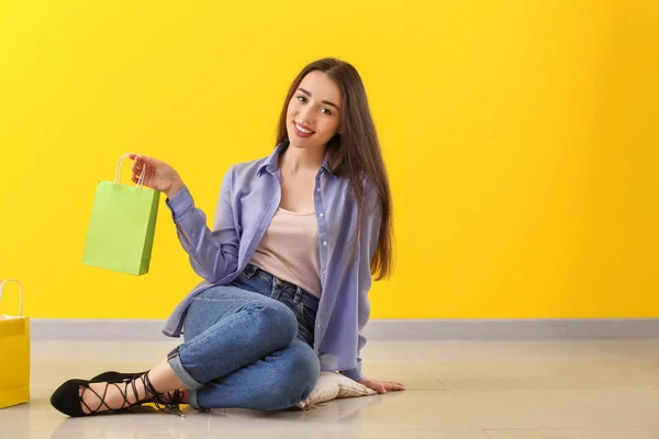 Gelukkige jonge vrouw met boodschappentassen zittend op de vloer in de buurt van Color Wall — Stockfoto