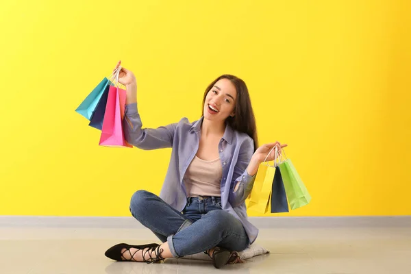 Happy young woman with shopping bags sitting on floor near color wall — Stock Photo, Image