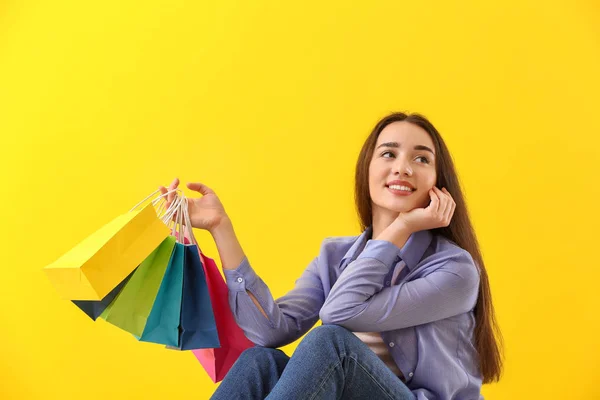 Happy young woman with shopping bags on color background — Stock Photo, Image