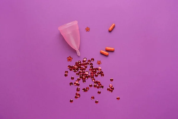 Menstrual cup, pills and red sequins on color background — Stock Photo, Image