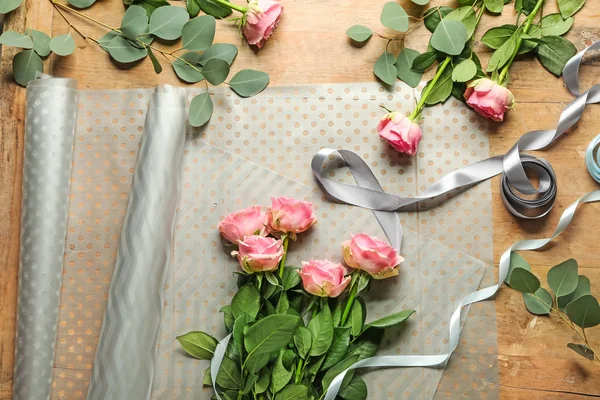 Vackra blommor med band och omslagspapper på träbord — Stockfoto
