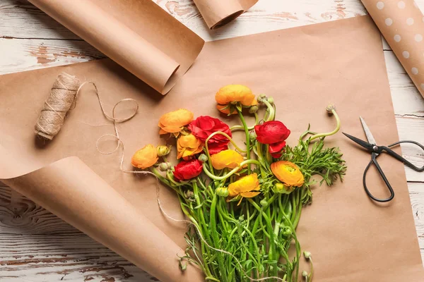 Beautiful flowers with scissors and wrapping paper on wooden table — Stock Photo, Image