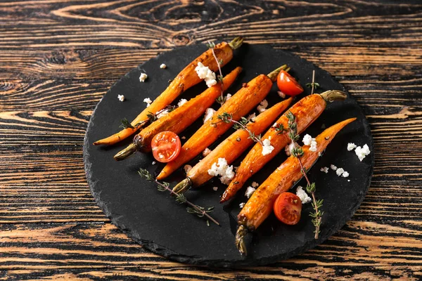 Slate plate with cooked carrot on wooden table