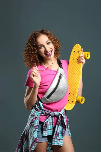 Stylische junge Frau mit Skateboard auf grauem Hintergrund — Stockfoto