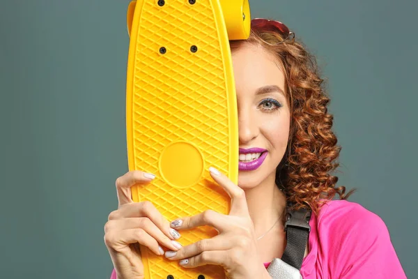 Стильная молодая женщина со скейтбордом на сером фоне — стоковое фото