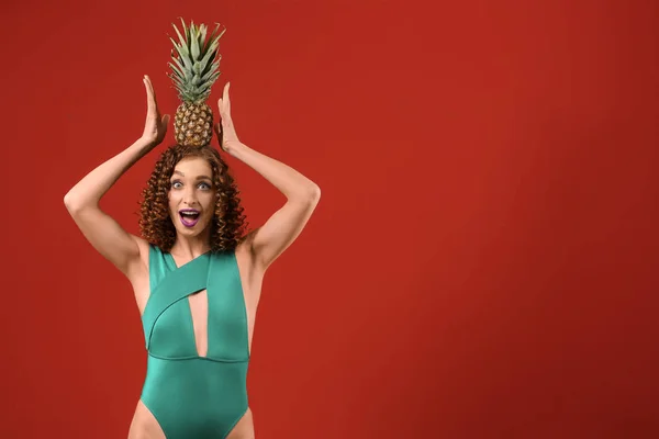 Emotional young woman in swimsuit and with tasty pineapple on color background — Stock Photo, Image