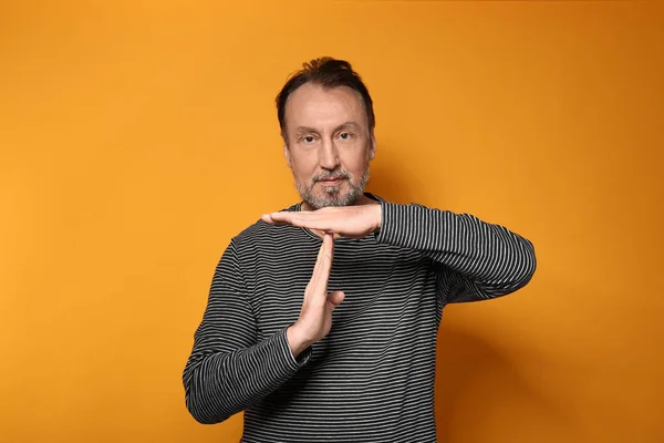 Portrait of handsome mature man showing time-out gesture on color background — Stock Photo, Image