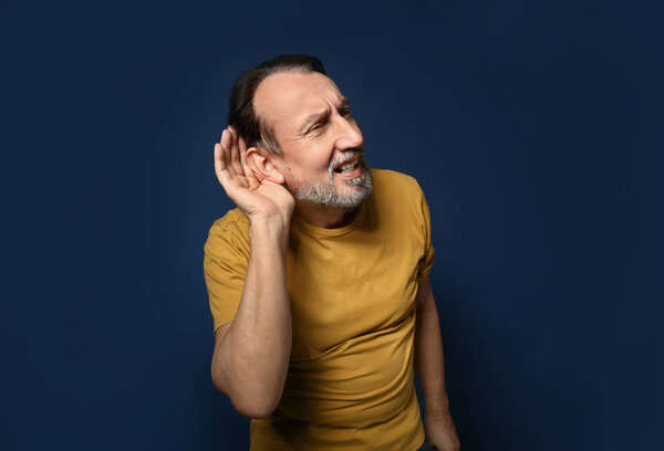 Портрет красивого зрелого мужчины с проблемами со слухом на цветном фоне
