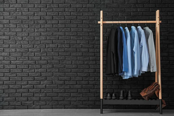 Estante con ropa masculina elegante cerca de la pared de ladrillo oscuro —  Fotos de Stock