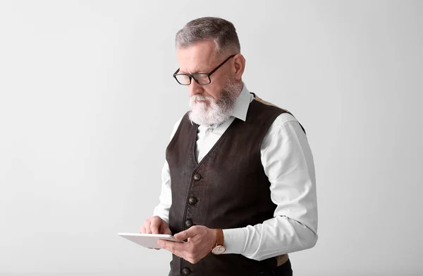 Knappe volwassen zakenman met Tablet computer op lichte achtergrond — Stockfoto