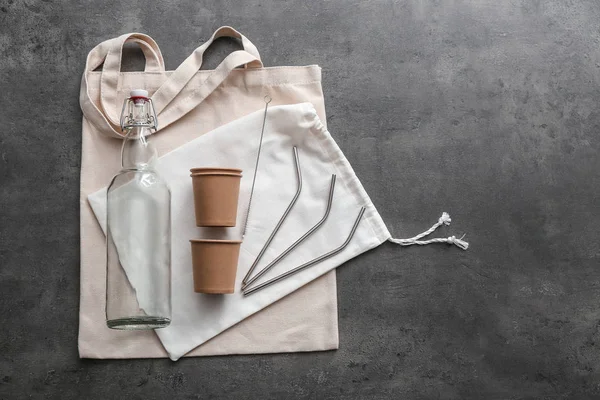 Glass bottle with bags, cups and cocktail straws on grey background. Zero waste concept — Stock Photo, Image