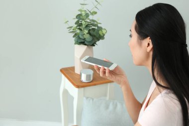 Odada cep telefonu olan asyalı genç bir kadın. Modern teknoloji ve akıllı ev otomasyonu