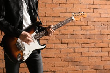 Yakışıklı genç adam tuğla duvara karşı gitar çalıyor