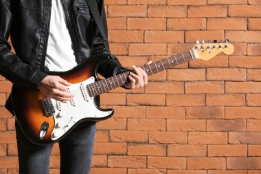Yakışıklı genç adam tuğla duvara karşı gitar çalıyor