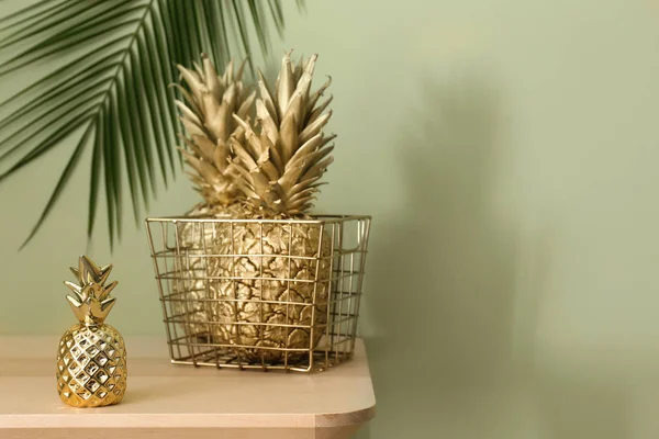 Košík se zlatými ananasy na stole proti zelenému pozadí — Stock fotografie