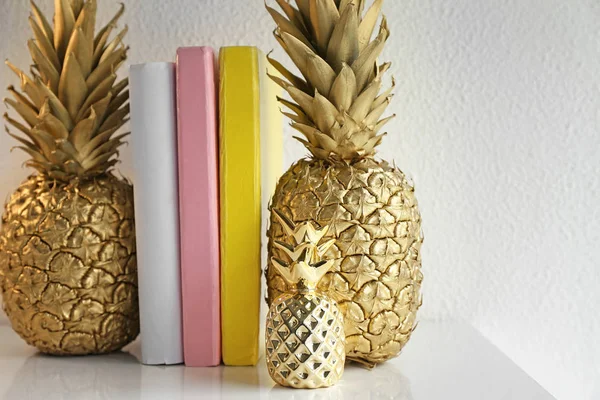 Golden pineapples with books on table near white wall — Stock Photo, Image