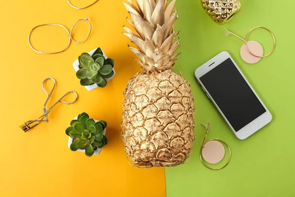 Golden pineapple with mobile phone, plants and female accessories on color background — Stock Photo, Image