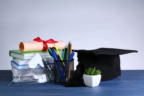 Mortar board, diploma, stationery and books on table. Concept of high school graduation