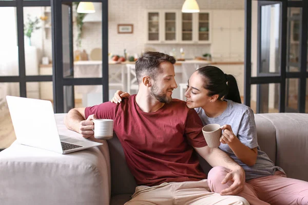 Feliz pareja joven con portátil bebiendo té en casa —  Fotos de Stock