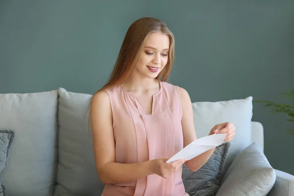 Young woman opening envelope with invitation at home