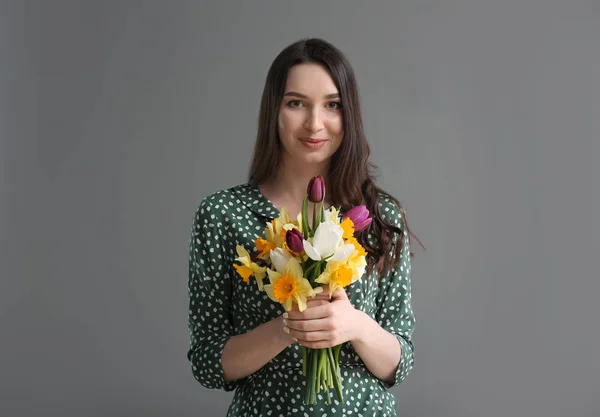 Beautiful young woman with bouquet of flowers on grey background — Stock Photo, Image