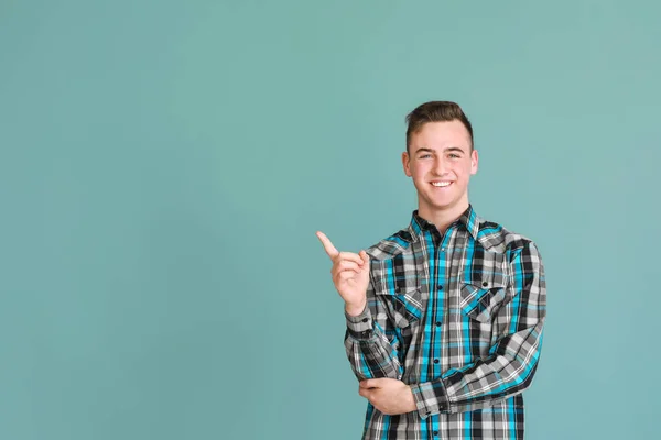 Cute teenage boy pointing at something on color background — Stock Photo, Image