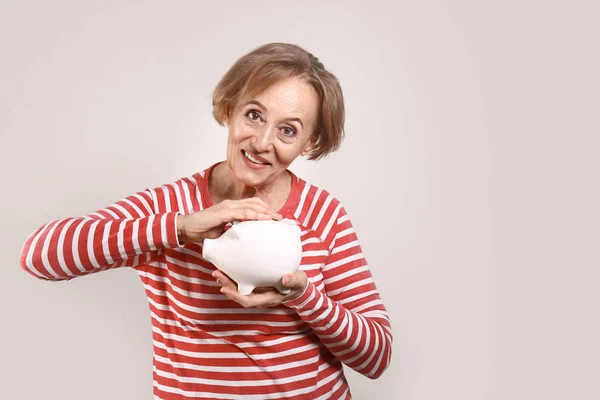 Hermosa mujer madura con alcancía sobre fondo gris — Foto de Stock