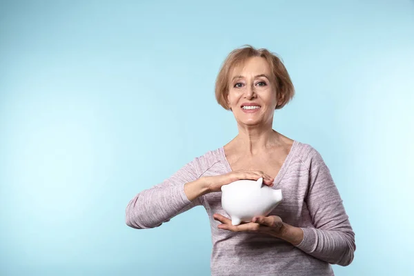 Schöne reife Frau mit Sparschwein auf farbigem Hintergrund — Stockfoto