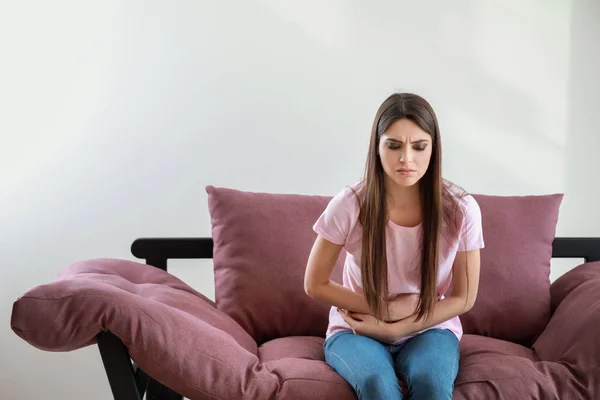 Young woman suffering from abdominal pain while sitting on sofa against white background — Stock Photo, Image