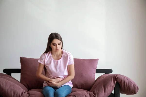 Young woman suffering from abdominal pain while sitting on sofa against white background — Stock Photo, Image