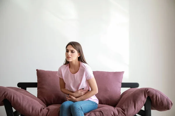 Young woman suffering from abdominal pain while sitting on sofa against white background — Stock Photo, Image