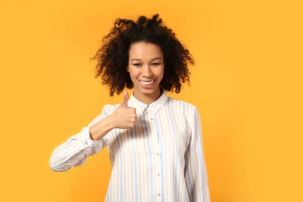 Happy African-American woman showing thumb-up gesture on color background — Stock Photo, Image