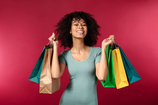 Happy African-American woman with shopping bags on color background — Stock Photo, Image