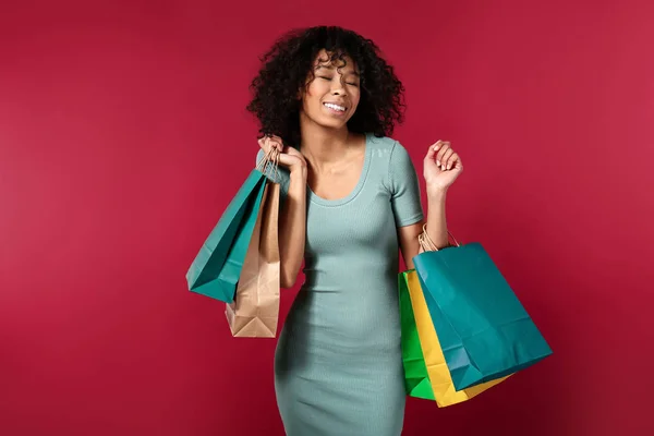 Šťastná afroameričanka s nákupními taškami na barevném pozadí — Stock fotografie